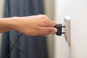 hand insetring, plugging or unplugging eclectrical wall outlet; concept of energy usage,...