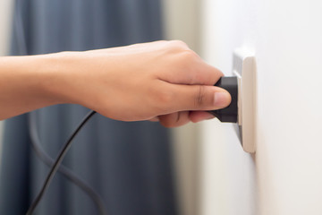 hand insetring, plugging or unplugging eclectrical wall outlet; concept of energy usage,...