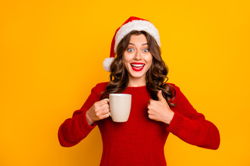 Pretty lady holding hot beverage in hands advising cool drink wear knitted jumper and santa hat isolated yellow background