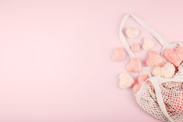 Reusable shopping net bag with white and pink knitted hearts on pastel background. Top view of eco friendly mesh shopping cotton bag. Ecological, Zero waste, No plastic concept