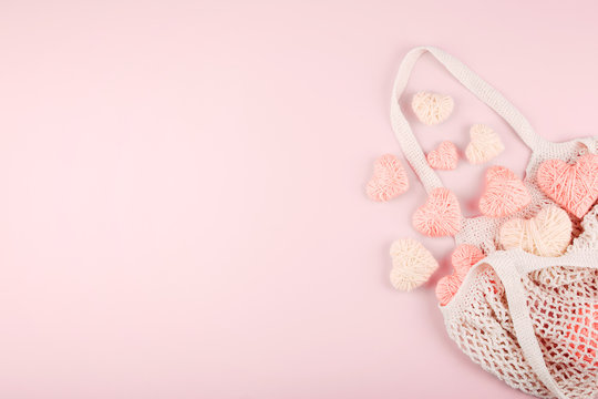 Reusable shopping net bag with white and pink knitted hearts on pastel background. Top view of eco friendly mesh shopping cotton bag. Ecological, Zero waste, No plastic concept