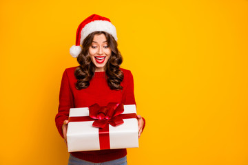 Pretty lady holding large giftbox in arms wear knitted pullover and santa hat isolated yellow background