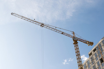 A yellow high-rise building crane against a blue sky builds multi-storey apartment buildings using modern technologies of metal, concrete and brick according to an architectural project