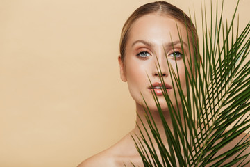 Blonde woman posing naked with green nature leaf plant.