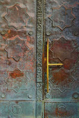 Fragment of an old door in a patina, covered with copper sheets with an ornament.