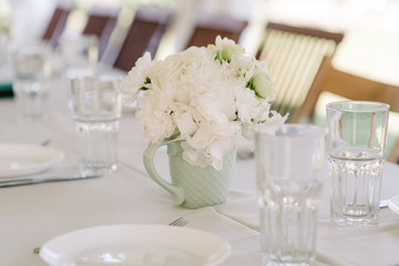 A bouquet of white gentle roses in a small mug-style vase.