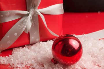 Red Christmas glass bauble with gift wrapped present on red and white fake snow background 