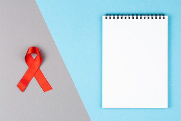 red aids ribbon on open notebook isolated on blue and gray background