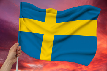 hand holds against the background of the sky with clouds the colored flag of Sweden on a luxurious texture of satin, silk with waves, closeup, copy space
