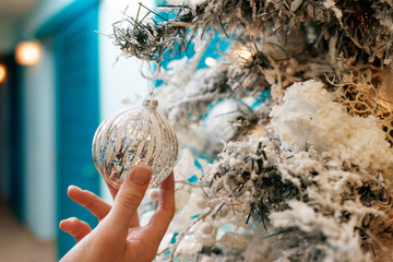 Hands decorating christmas tree with a silver balls.