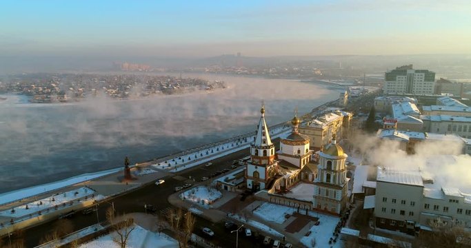 Aerial: Drone moving over Sobor Bogoyavlensky by vehicles on street and snow covered promenade - Irkutsk, Russia