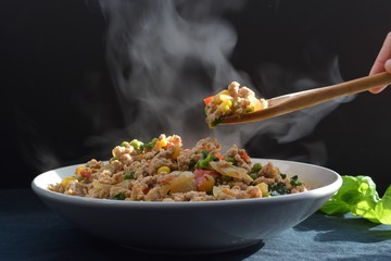 Dish with fried chicken chili, garlic, onions, basil and green peas with rice with a wooden spoon in front of a black background