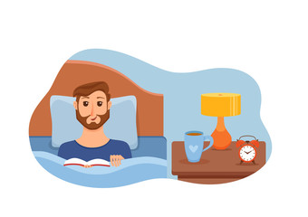 Guy lying on bed in home bedroom and reading a book in her hands under lamp light