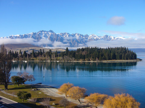 Landscape image of a snowy mountain, overlooking the lake with different colored trees in view