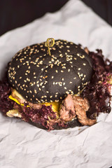 black bread burger with healthy meat and leaves of brown salad on paper