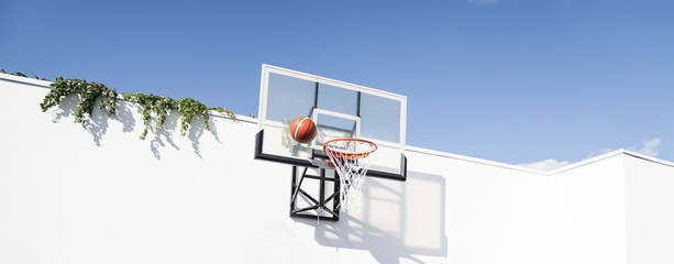 basketball hoop on a white blank wall in the yard against the summer sky and a basketball.