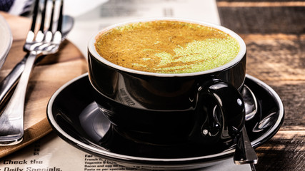 A close up view of a chai latte in a cup and saucer on a wooden table.