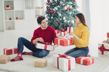 Obraz na płótnie Canvas Full size profile side photo of two romantic people hold gift box get presents from santa claus sit on floor in house with evergreen tree x-mas noel decoration