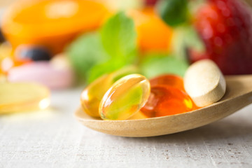 Colorful pills and capsules in wooden spoon with fresh fruits.Vitamins and supplement from fruits concept.
