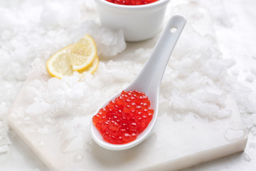 Spoon with red caviar and ice on white board