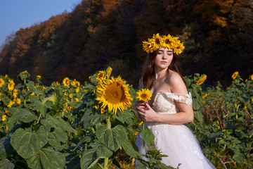 Beautiful cute sexy girl in a white dress with a wreath of sunflowers on her head enjoying nature....