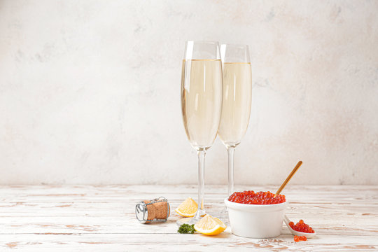Bowl with red caviar, lemon and glasses of champagne on white wooden table