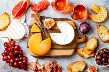 Appetizers, antipasti snacks and rose wine in glasses. Cheese and meat platter on wooden board over grey concrete background. Top view