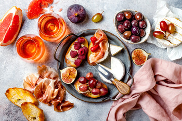 Appetizers, antipasti snacks and rose wine in glasses. Bruschetta or authentic traditional spanish tapas set, cheese and meat platter over grey concrete background. Top view