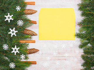Fir tree branch with cinnamon, cones, snowflakes, yellow envelope on wooden background. Christmas and New Year concept
