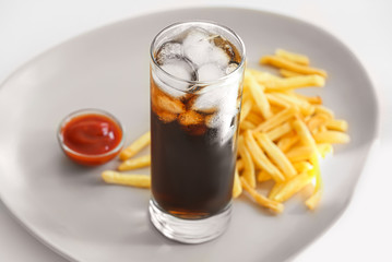 Glass of cold cola with french fries on plate