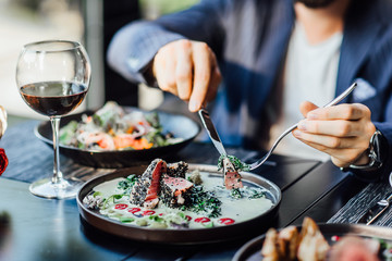 Portrait of man eating strip steak served with loaded baked potato and broccoli at restaurant table.