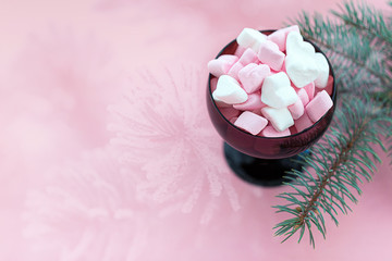 White and pink marshmallows in bowl on pink background. Fir branches. Happy new year. Space for creativity