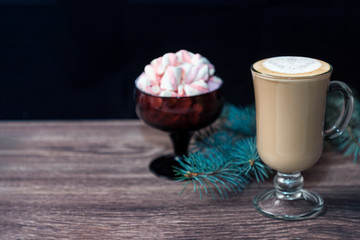 A Cup of hot chocolate with marshmallows on a wooden table. A glass glass of sweet winter cocoa and a fir branch. Happy new year