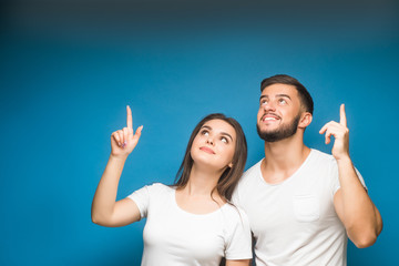 Happy casual couple pointing up to something on blue background, copy space.