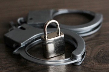 the silver handcuffs and metal lock on wooden background
