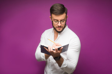 Portrait of cheerful businessman making notes isolated on violet background.