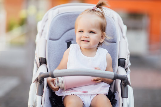 Small pretty girl sitting in a stroller, baby for a walk in a pram, child in summer outdoors.