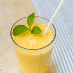 Blended smoothie on table. yellow juice on blue textile background. Fresh organic smoothie, healthy drink with fresh fruit. square format.