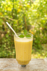 Blended smoothie with ingredients on wooden table. yellow juice on green leaves background. Fresh organic smoothie, healthy drink with fresh fruit.