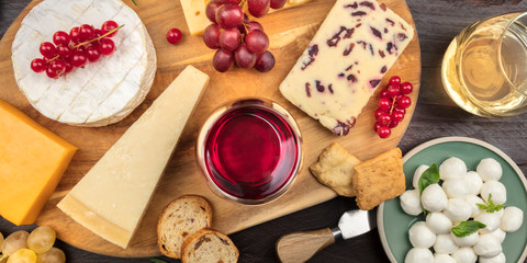 Cheese panorama. Camembert, Cheddar, Parmesan, etc, shot from the top on a dark rustic wooden background with wine and fruit