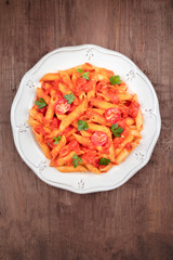Penne pasta with tomato sauce and parsley, shot from above on a dark rustic wooden background with a place for text