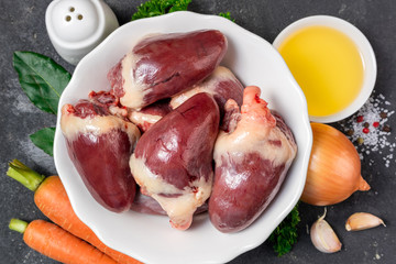 Raw turkey hearts with herbs and spices, vegetables carrots and onion on dark background. Ingredients for cooking hearts offal. Healthy food. Top view