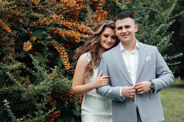 Fototapeta premium Young couple in celebrate outfits among the branches of sea buckthorn. Young woman and man smiling and having fun together. Happy lovers and family. A loving couple, a guy and a girl