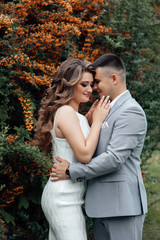 Beautiful wedding photos in summer. Beautiful young couple hugging  among the branches of sea buckthorn. Beautiful couple are walking in the park at summer. Beautiful young couple tenderly kissing