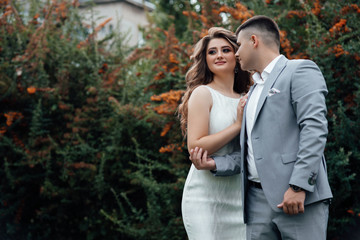 Young couple in love outdoor. Young couple in celebrate outfits among the branches of sea buckthorn. A loving couple, a guy and a girl kiss and hug. Happy lovers and family.  Love story. 