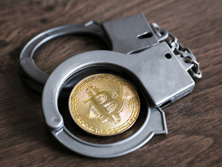 Gold bitcoin and handcuffs on a wooden table, cybercrime.