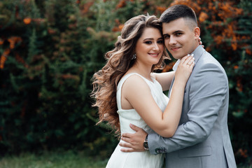 Newlyweds happily smile for a summer walk among the berries of sea buckthorn. Just married couple after ceremony. Loving couple among the branches of sea buckthorn, people's attitudes. Love story.