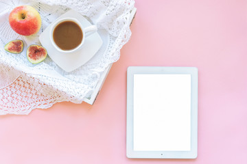 Tablet computer with blank screen and healthy breakfast on a tray, coffee or cocoa, apple and sliced figs, knitted napkin. Pink background, top view, flat lay, mock up, copy space.