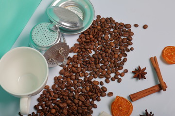 Coffee beans, cinnamon sticks, allspice and anise. Nearby is a white cup and slices of dried oranges. On white background. World Coffee Day.