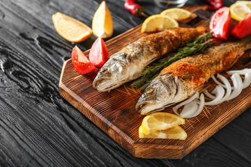 Board with tasty cooked seabass fish on dark table